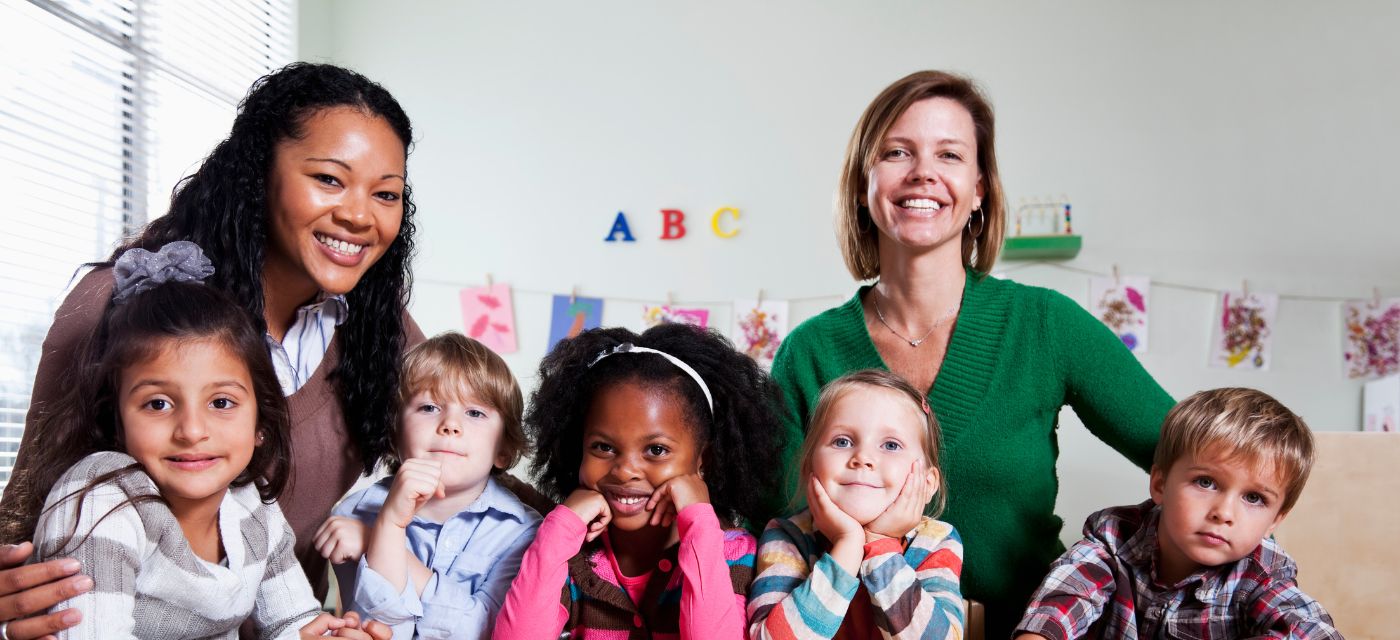 Group of young children with two teachers in classroom.